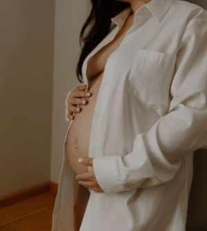 Minimalist maternity photo in white button-down shirt showing baby bump.