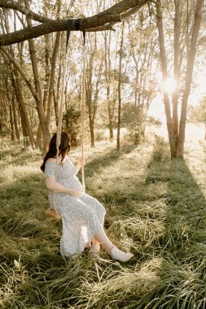 Dreamy sunset maternity photo in a wooded forest setting with streaming sunlight.