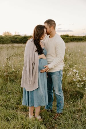 Tender maternity moment captured in a sunlit meadow with wildflowers and natural golden light.