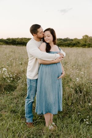 Intimate embrace in a serene meadow during golden hour showing expectant parents in soft lighting.