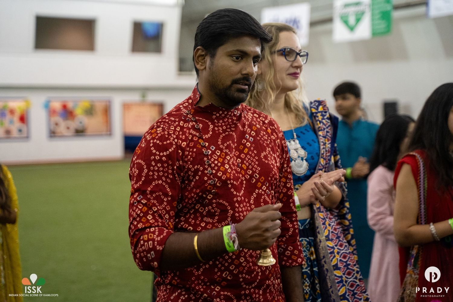 People gathered at an indoor cultural celebration wearing traditional Indian attire.