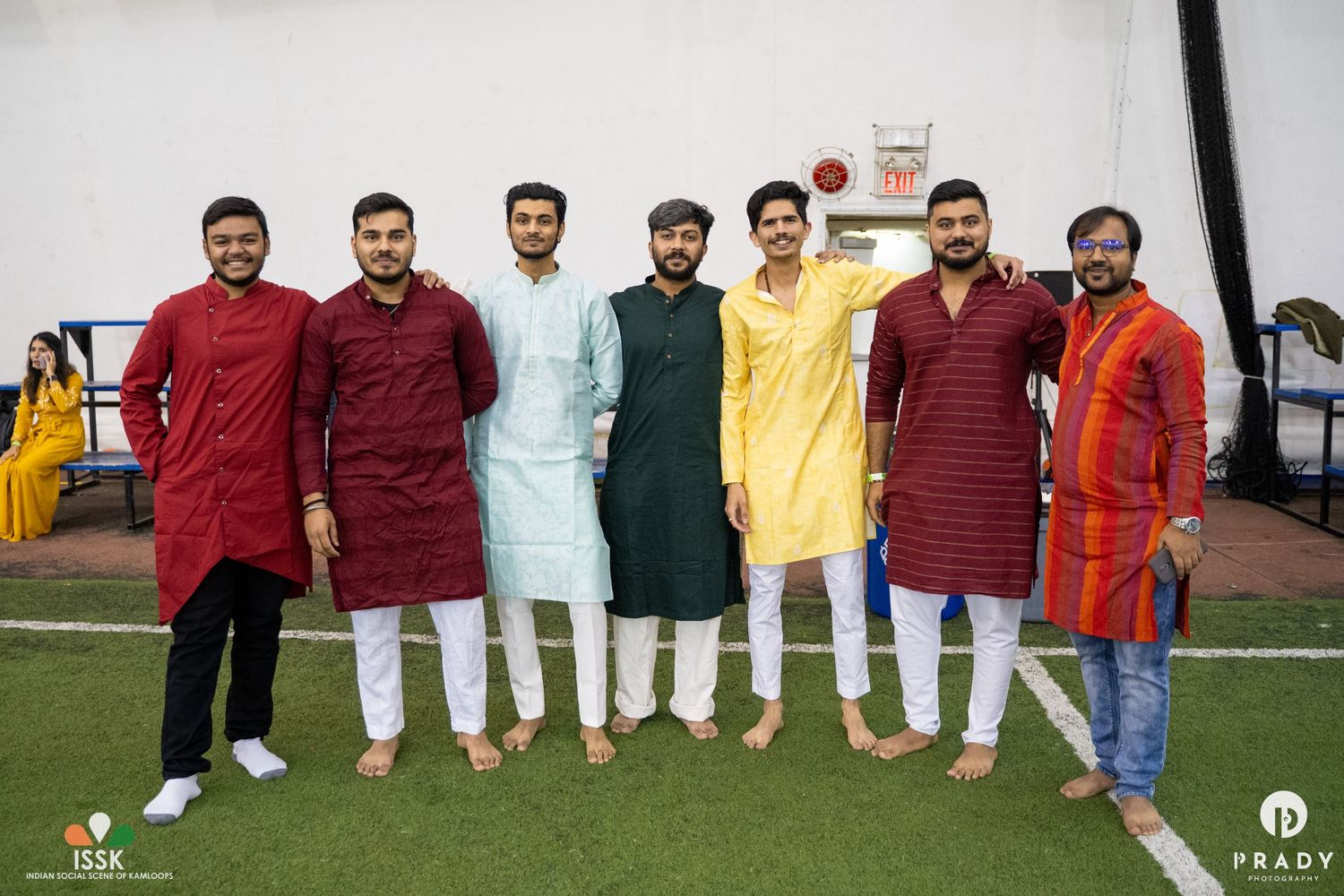 A group photo of men wearing traditional kurtas in various colors standing together on a green field.