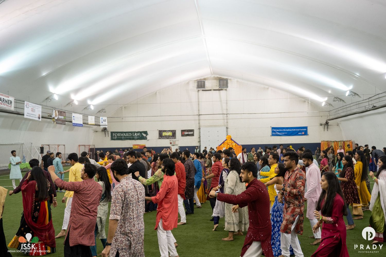 Large indoor celebration with colorfully dressed guests gathered in a white-domed event space.