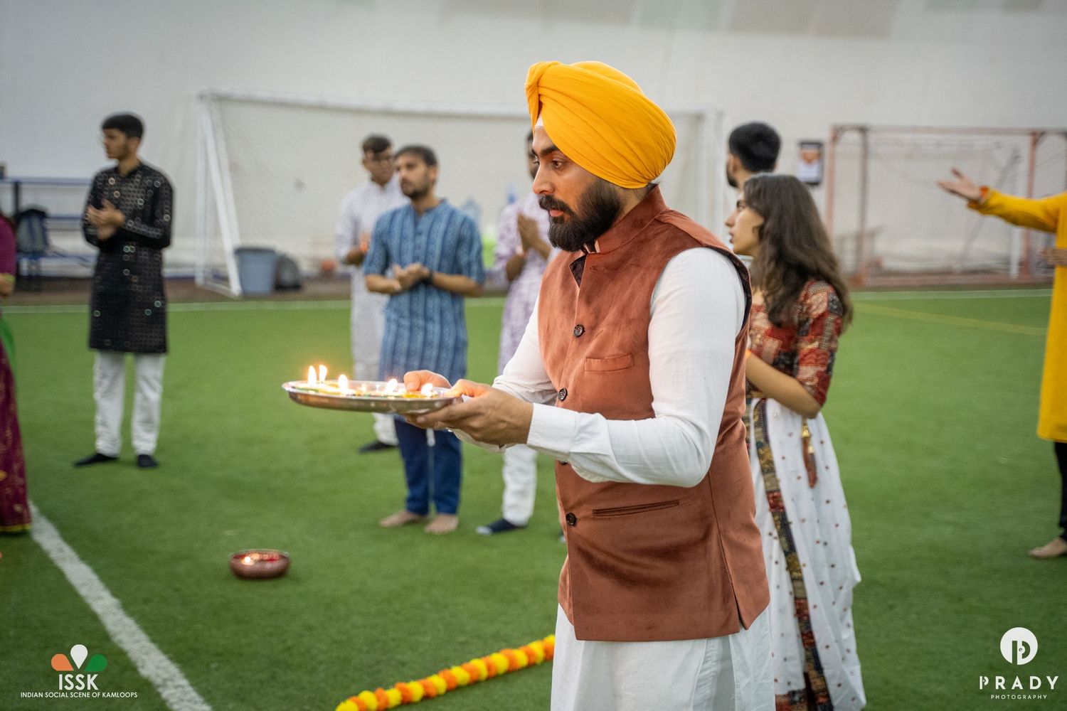 A person in a turban and brown vest holding a ceremonial plate during a cultural gathering.