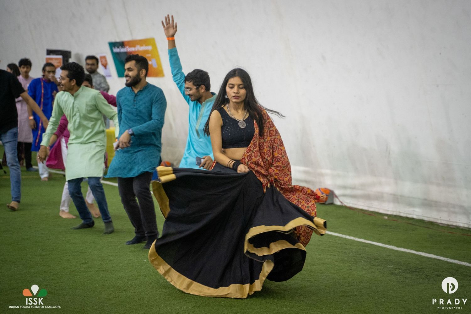 People dancing and celebrating in traditional Indian attire on an indoor sports field.