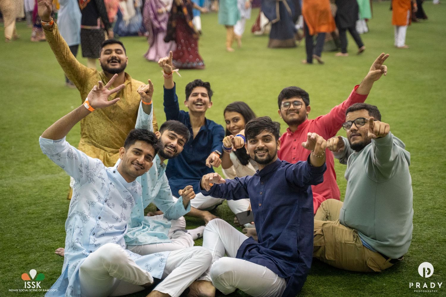 Group of friends posing together while sitting on grass during an outdoor festival.
