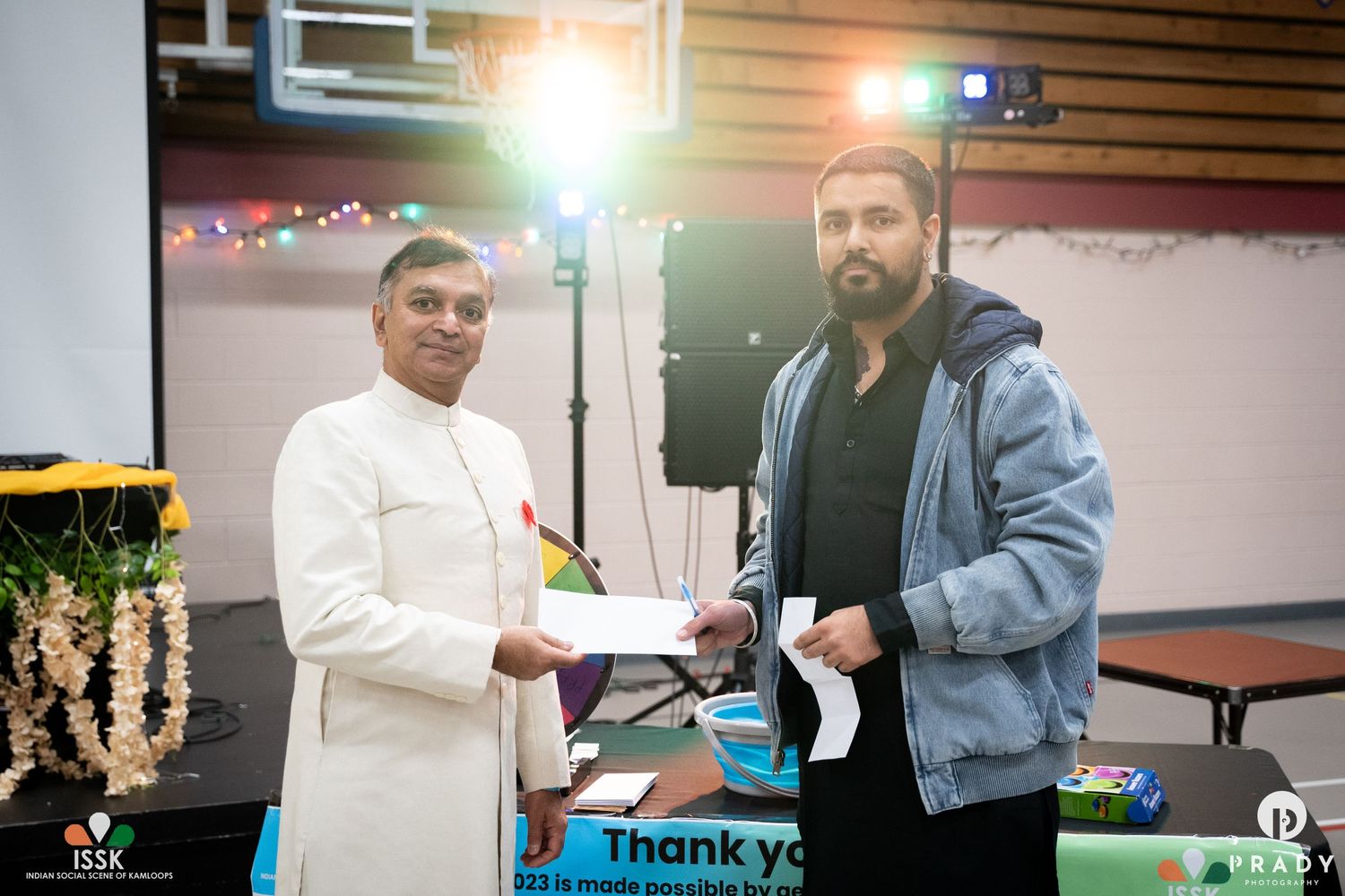 Two people exchanging documents at indoor event with pink wall background.