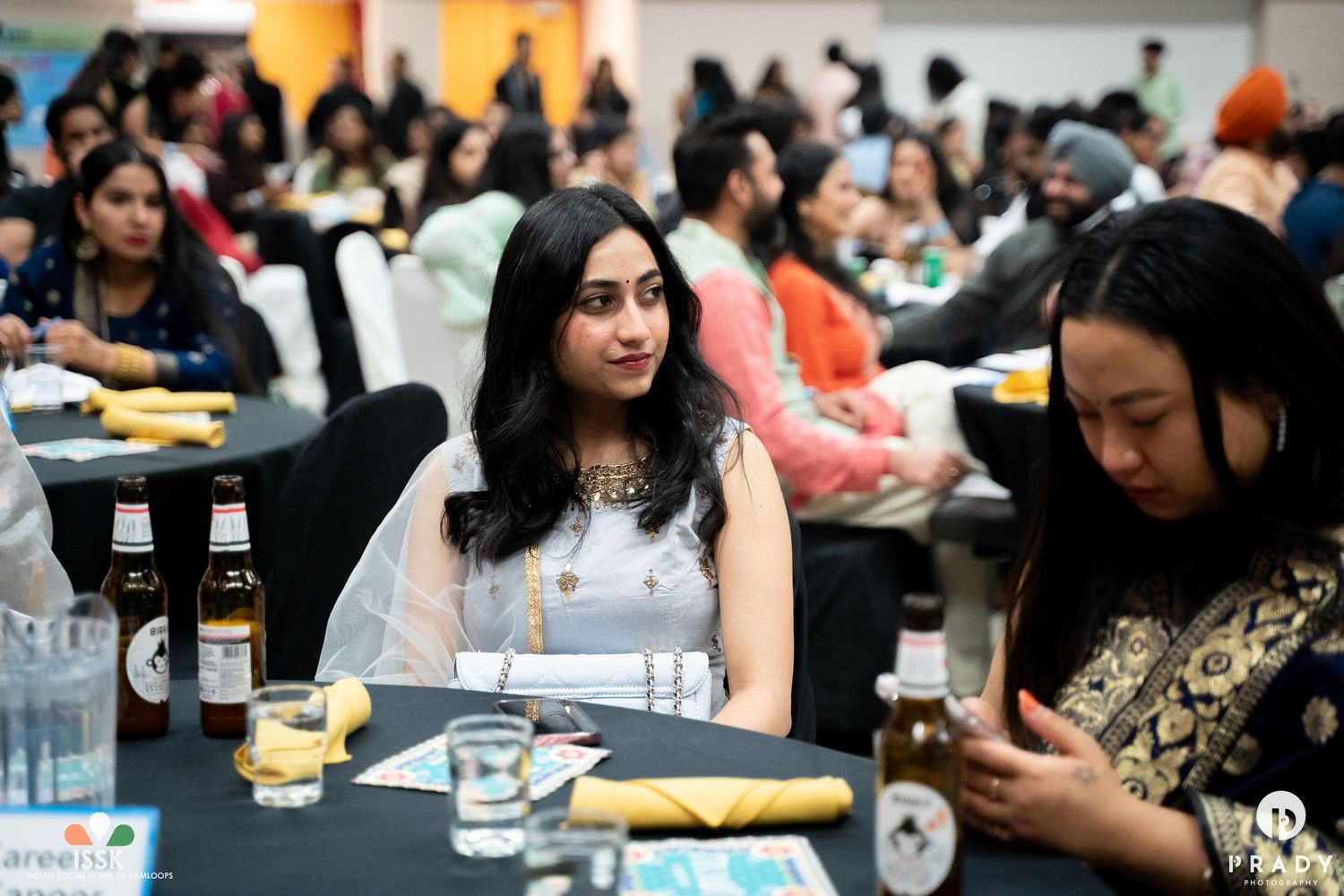People seated at dining tables during formal indoor event with beverages.
