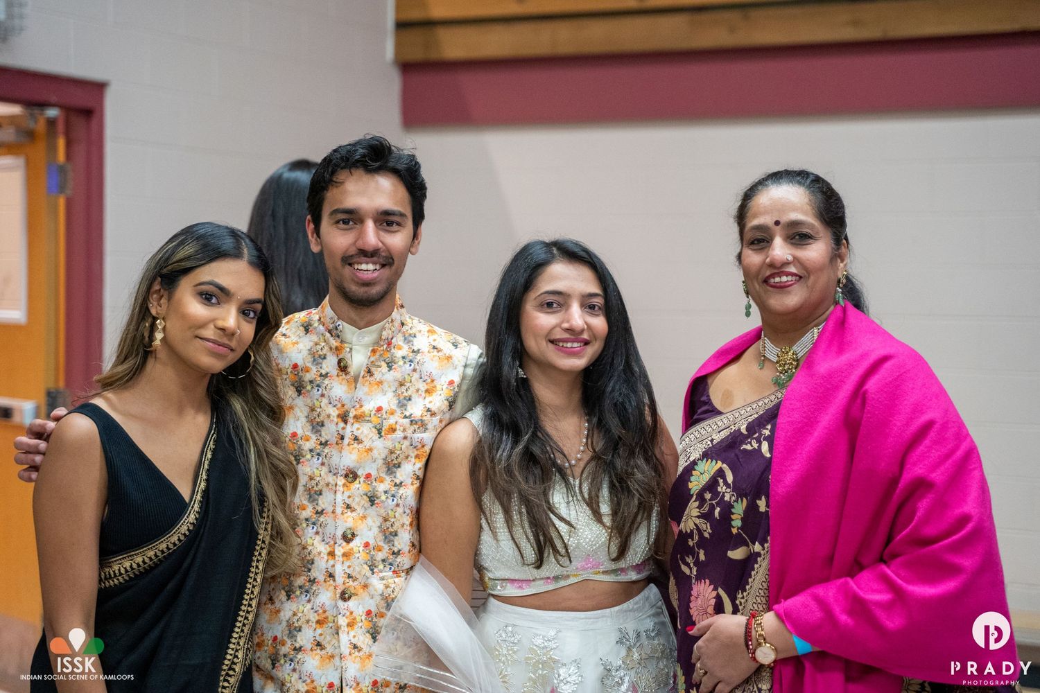 A group in festive attire poses together at a social gathering, with outfits including yellow floral and bright pink.