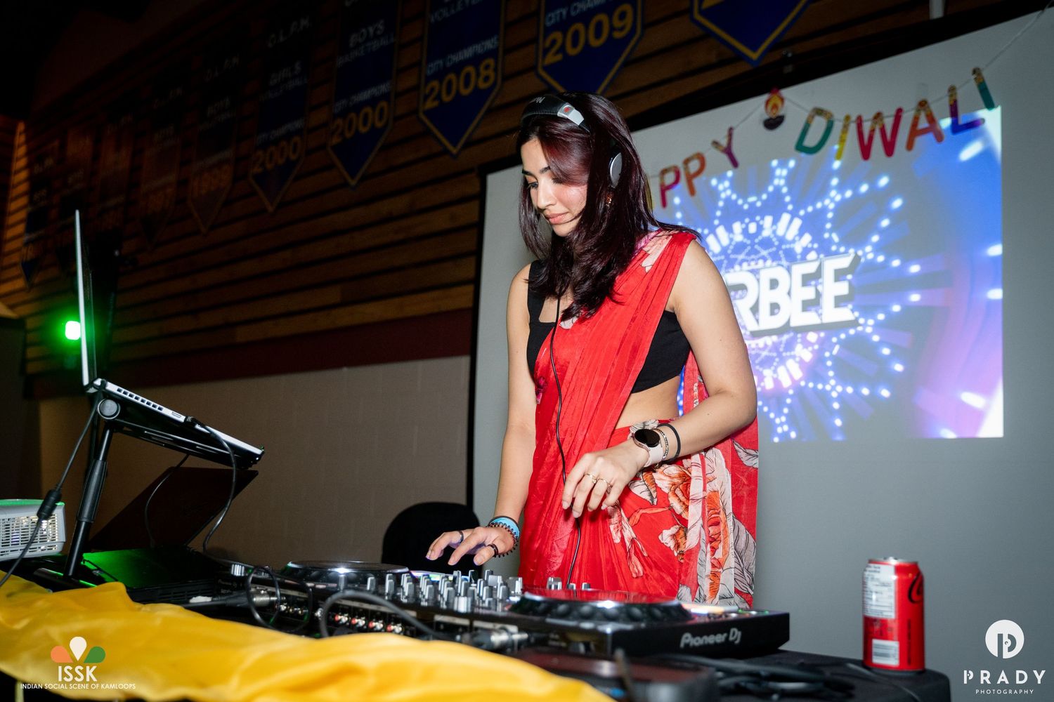 DJ performing in traditional red sari at a Diwali celebration event with equipment and lighting.