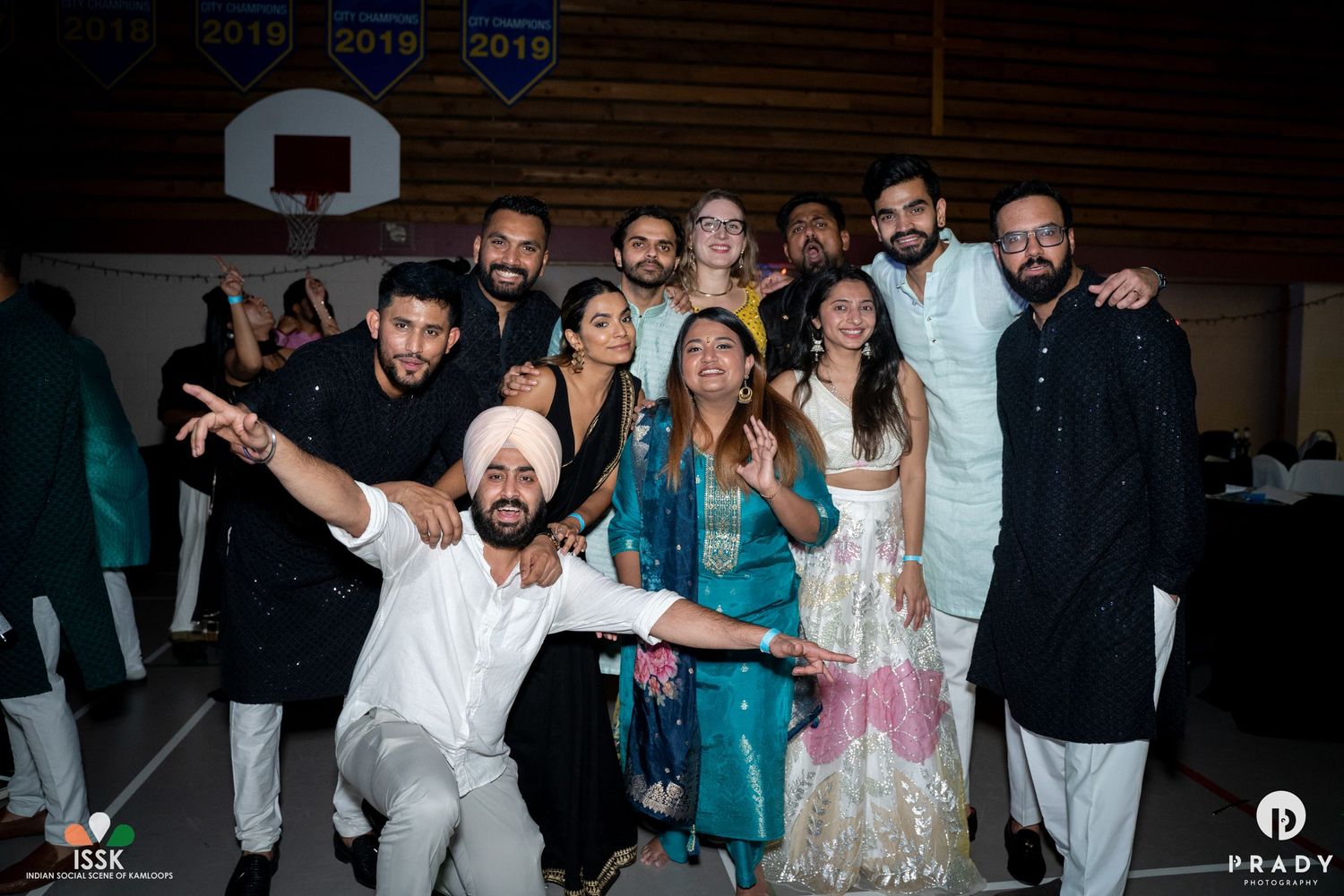 Party guests posing together in formal ethnic wear at an indoor celebration.