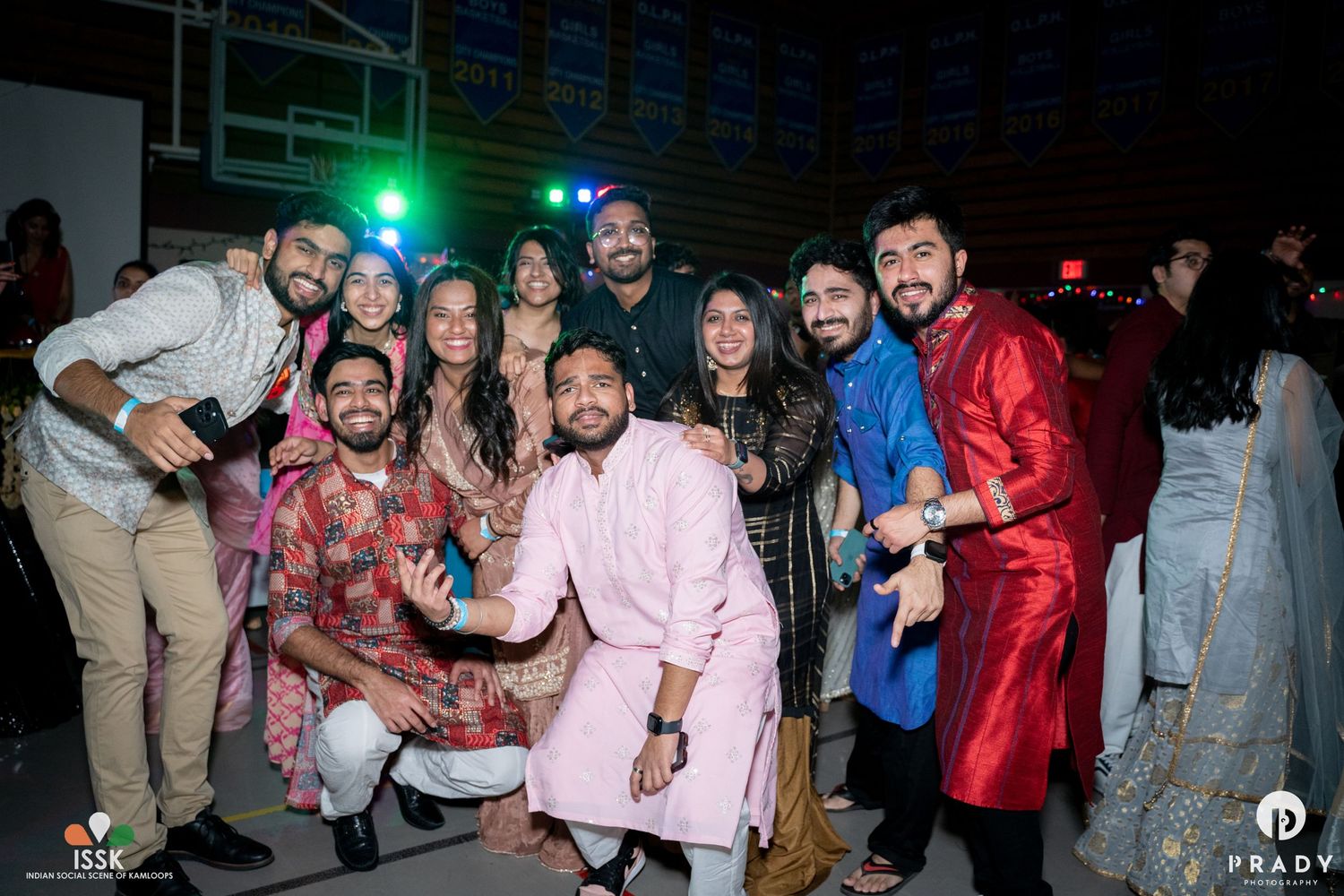 Large group celebrating at indoor party wearing mix of traditional and modern outfits.