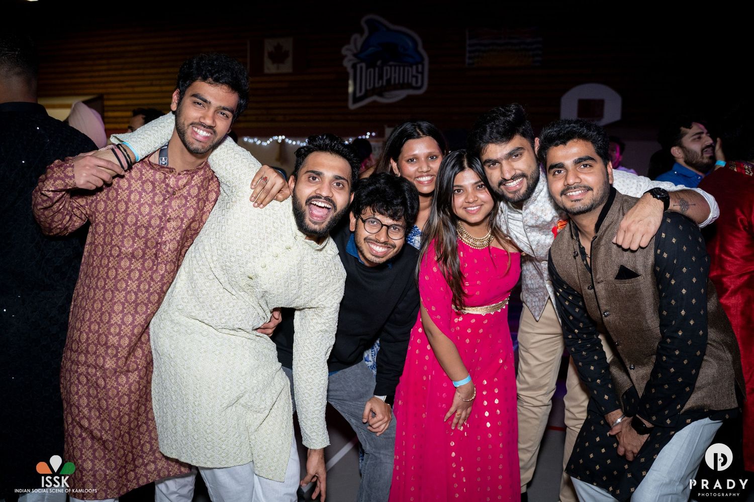 Party guests in traditional Indian attire posing together at indoor celebration.