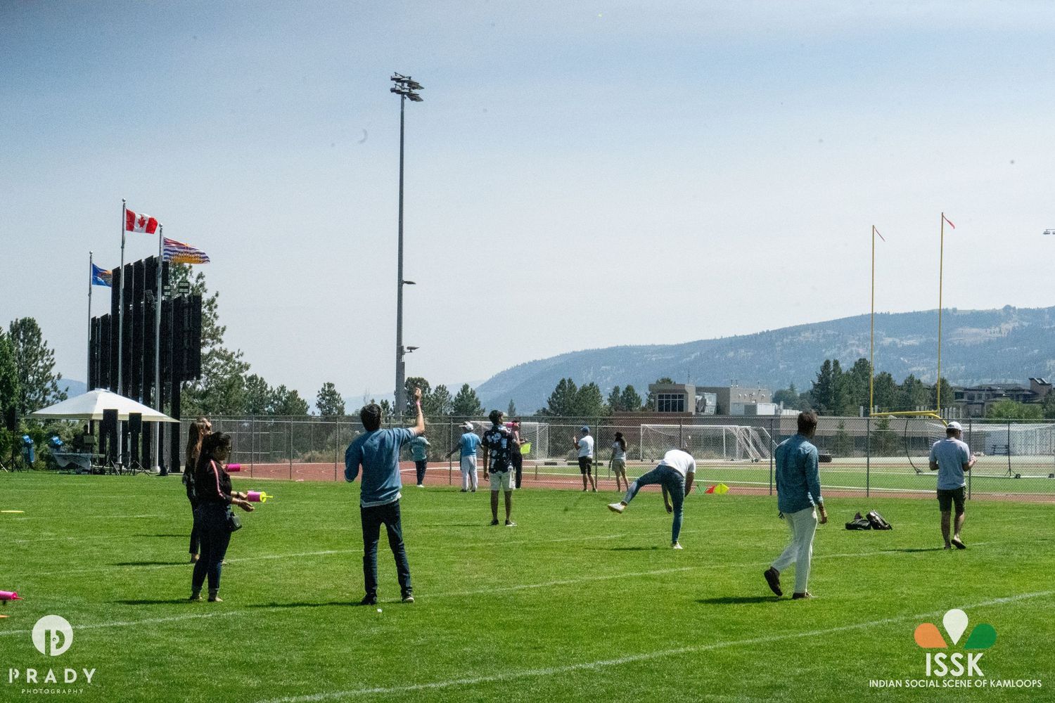 People playing games on a sports field with mountains visible in the background.