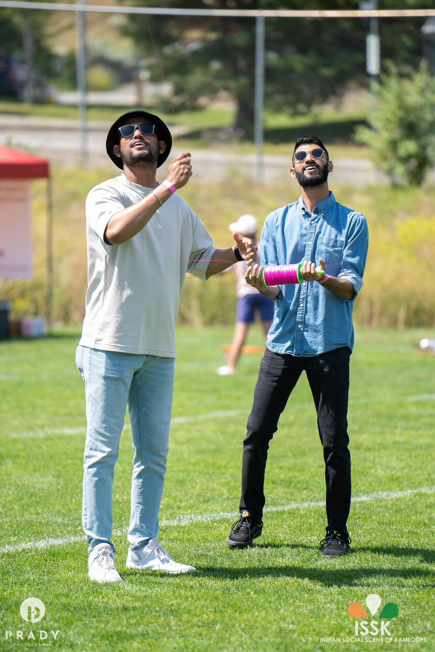 Two people flying kites on a sunny day in a grassy field.