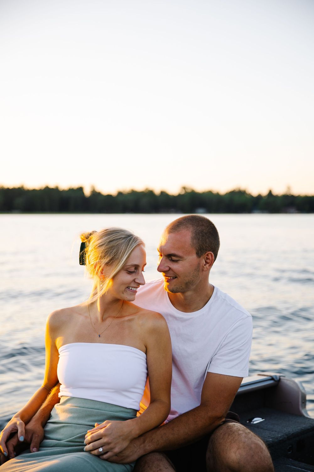 A couple sits together by a serene lake during golden hour.