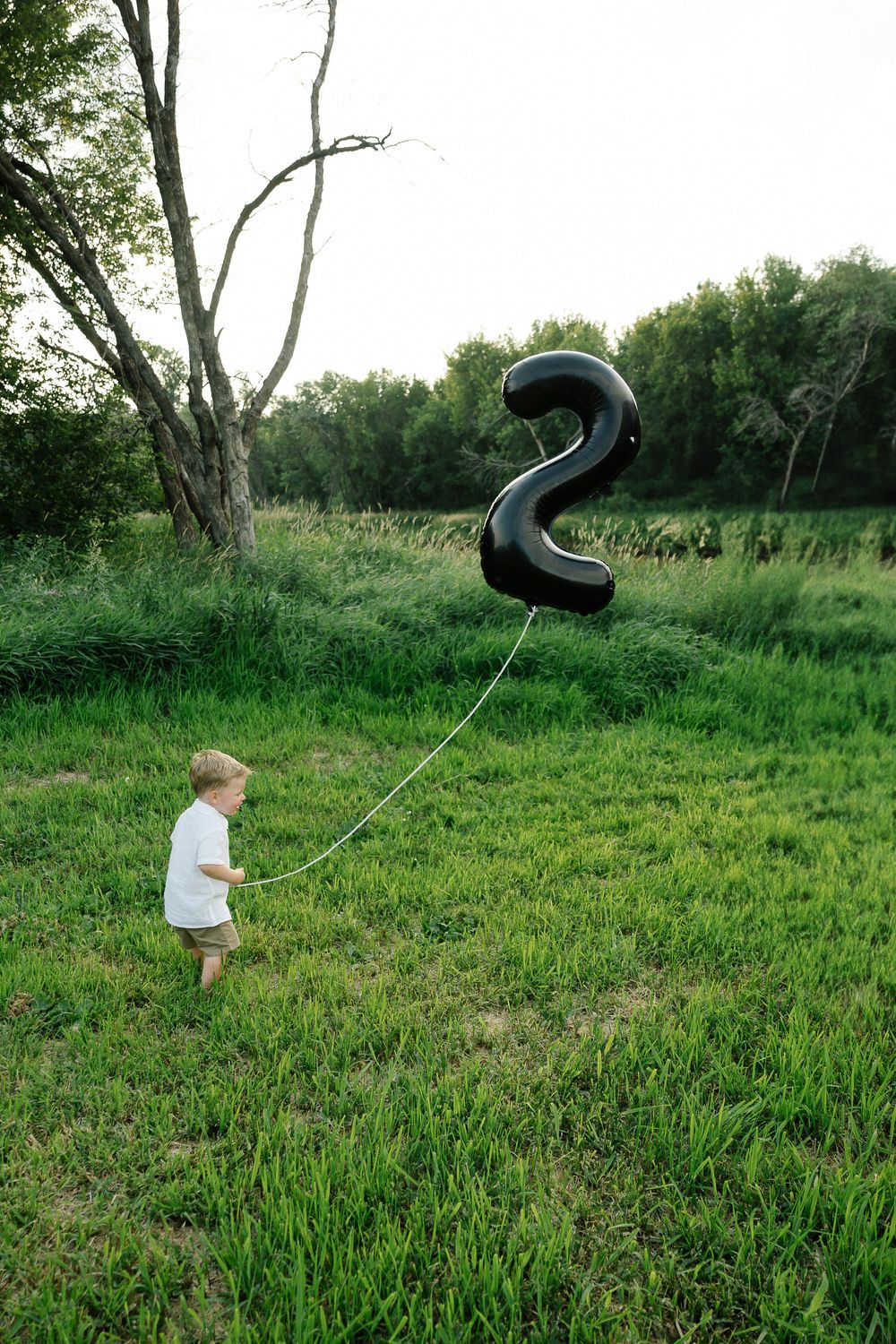 Small child holding string attached to black number 2 balloon in grassy field.