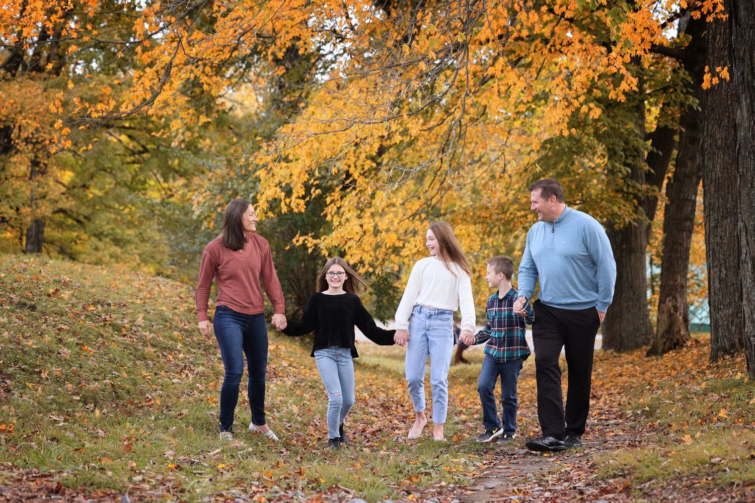 Family of five walking together on a path surrounded by vibrant fall foliage in Lifestyle family photo session.