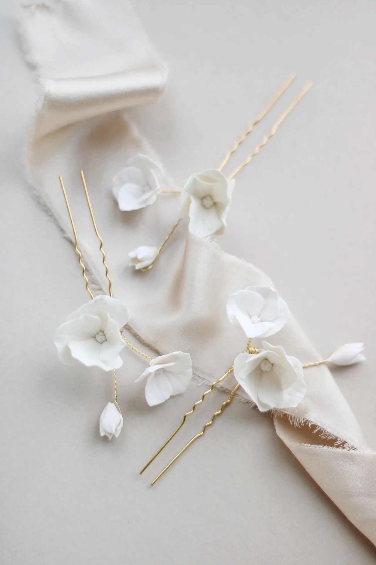 Elegant white floral hair pins with gold accents arranged on light gray surface.