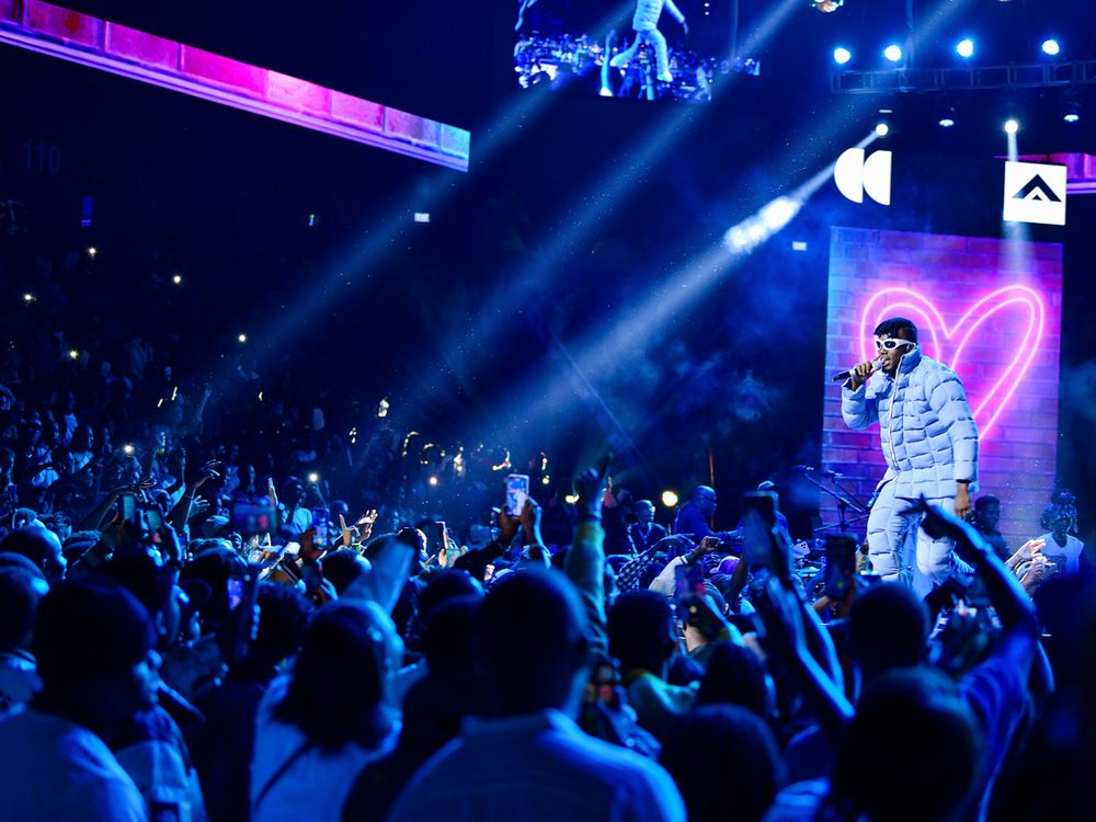 Concert venue filled with enthusiastic crowd while performer stands elevated with neon heart display.