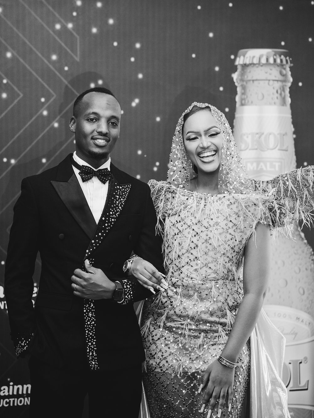 Formal couple posing against illuminated backdrop with decorative bottle display.
