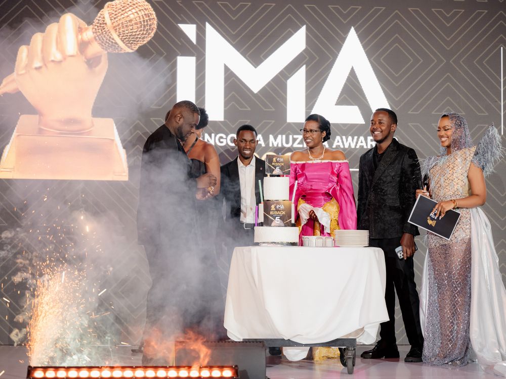 Group gathers around celebratory cake at IMA Awards with smoke effects.