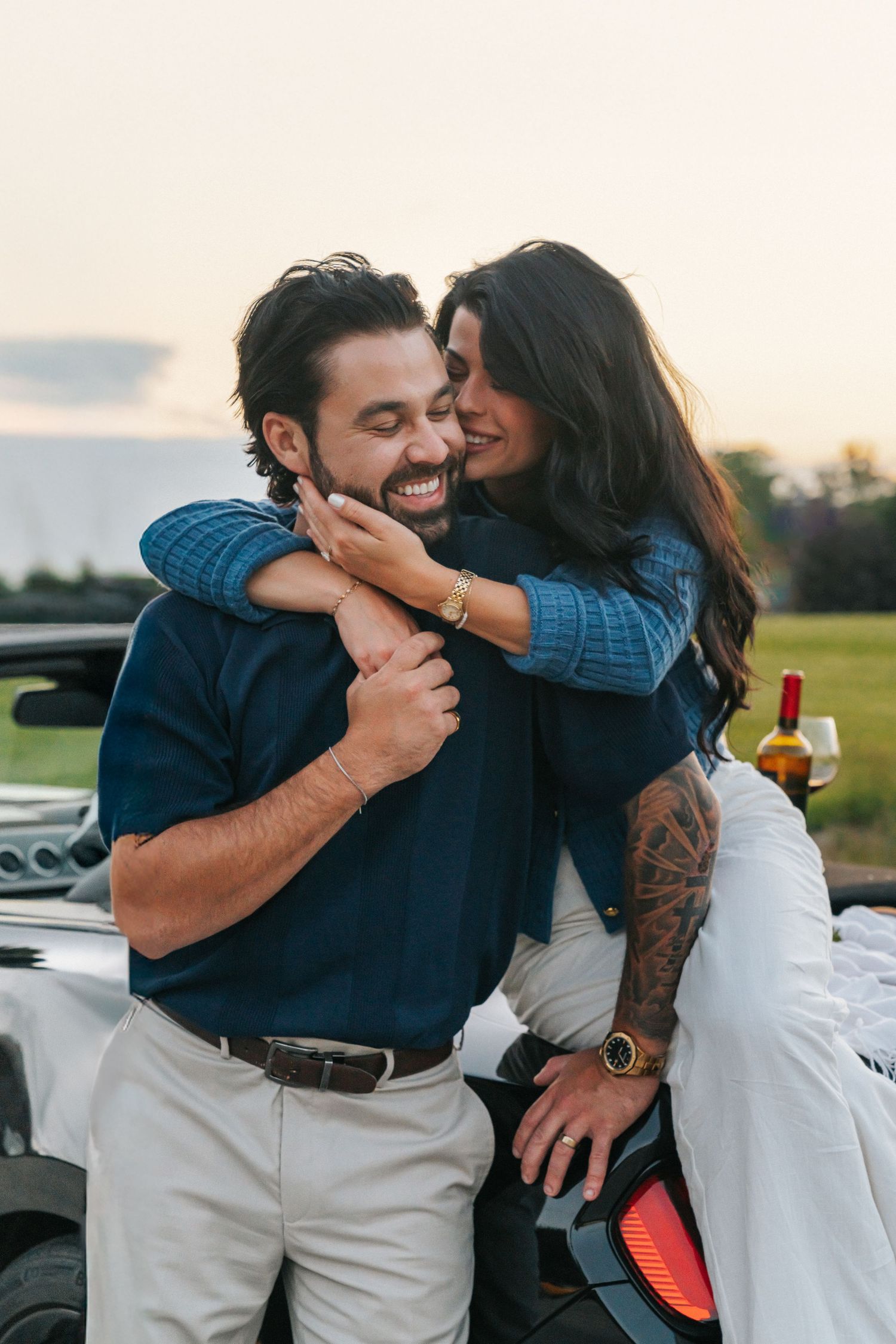 Romantic couple embraces and laughs together during sunset photo session in an outdoor setting.