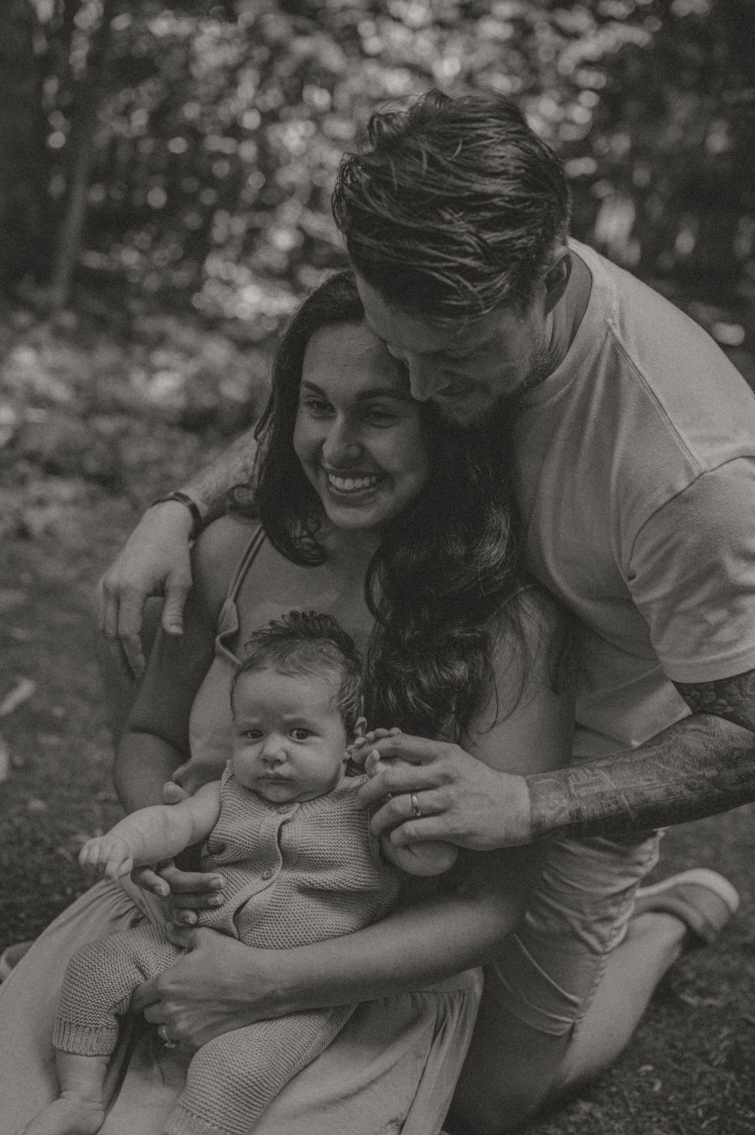 Black and white portrait by Samantha Campbell imagery of a happy family laughing together outdoors with a baby in a casual outdoor setting.