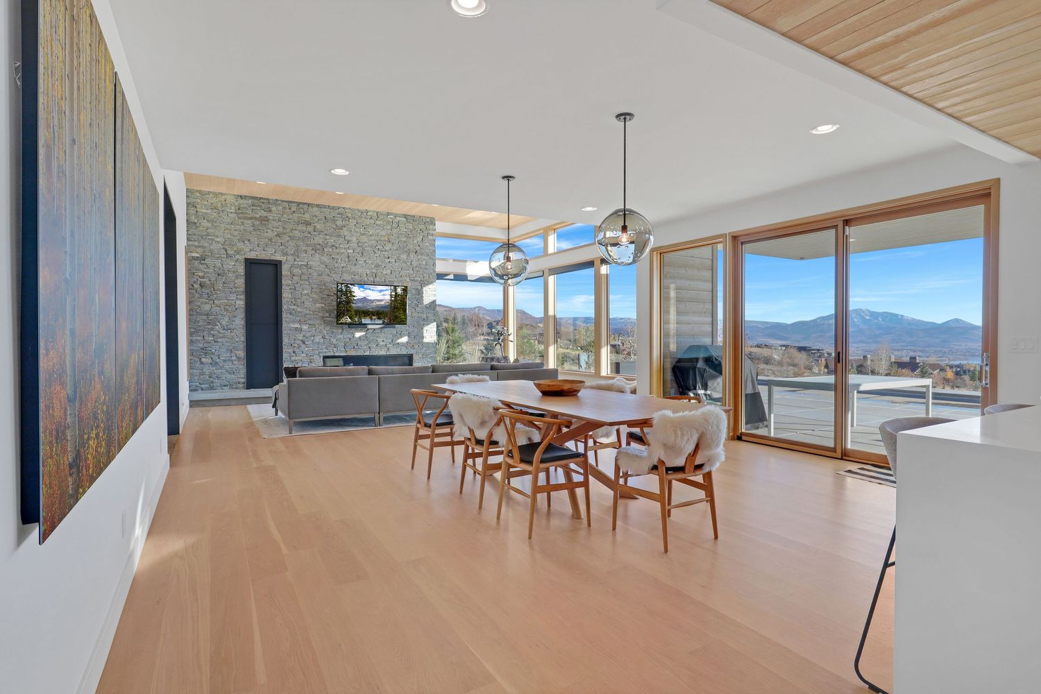 Modern dining room with mountain views, light wood floors, pendant lights, and open living area. Captured by Slate Media (best in UT)