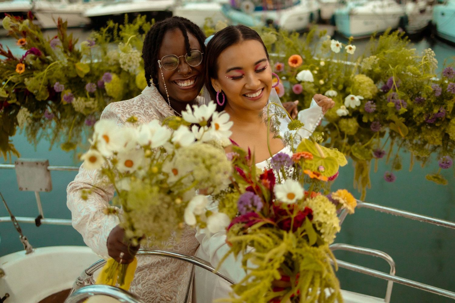 Happy couple holding floral bouquets outdoors surrounded by greenery.