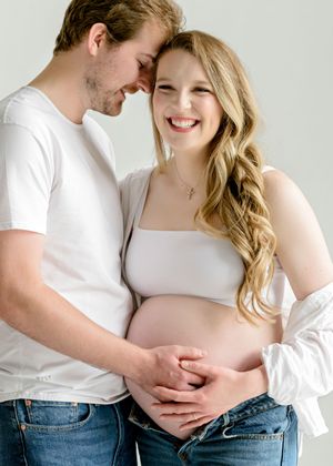 A loving couple shares an intimate moment while embracing and touching a pregnant belly in a bright studio setting.