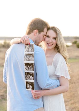 Couple holding ultrasound photos in a romantic outdoor setting during sunset with desert landscape in background.