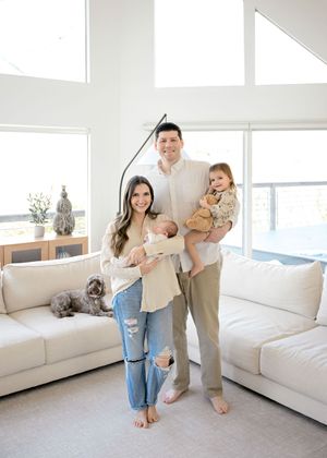 A family relaxes together in a bright modern living room with white furniture and large windows.
