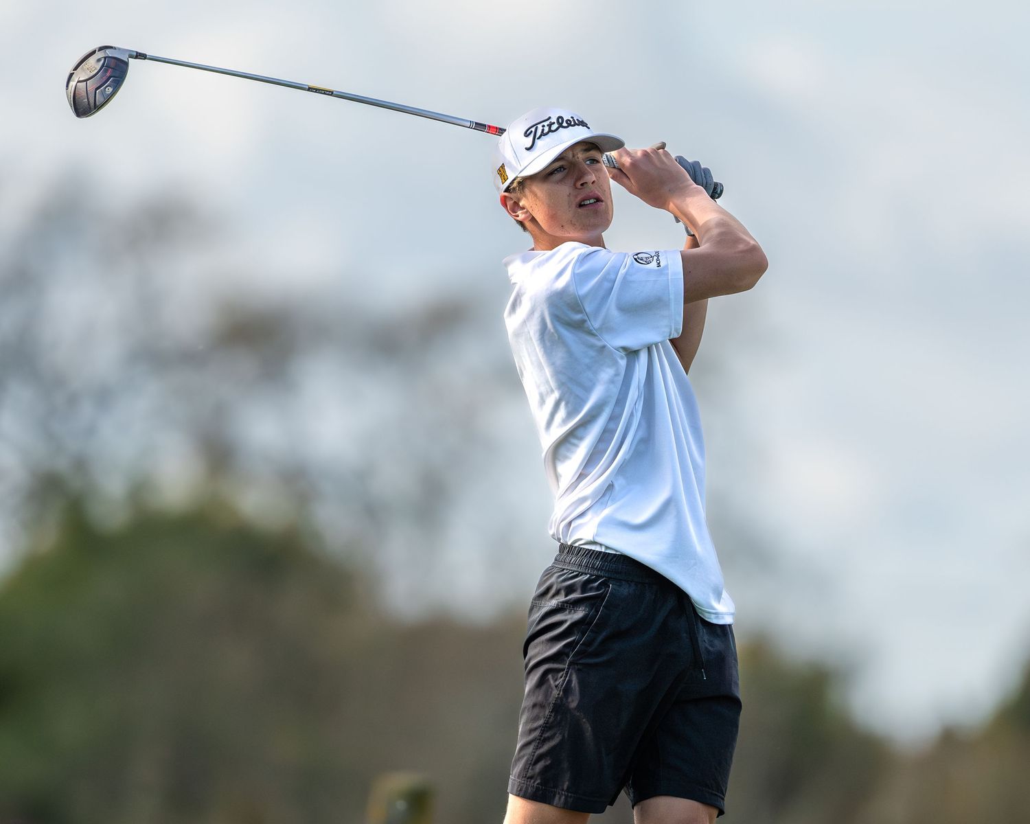 Golfer in white shirt following through on swing against light blue sky.
