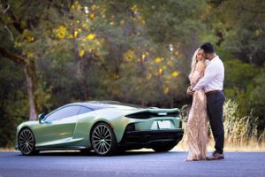 Romantic couple's photoshoot with luxury cars in background during golden hour.
