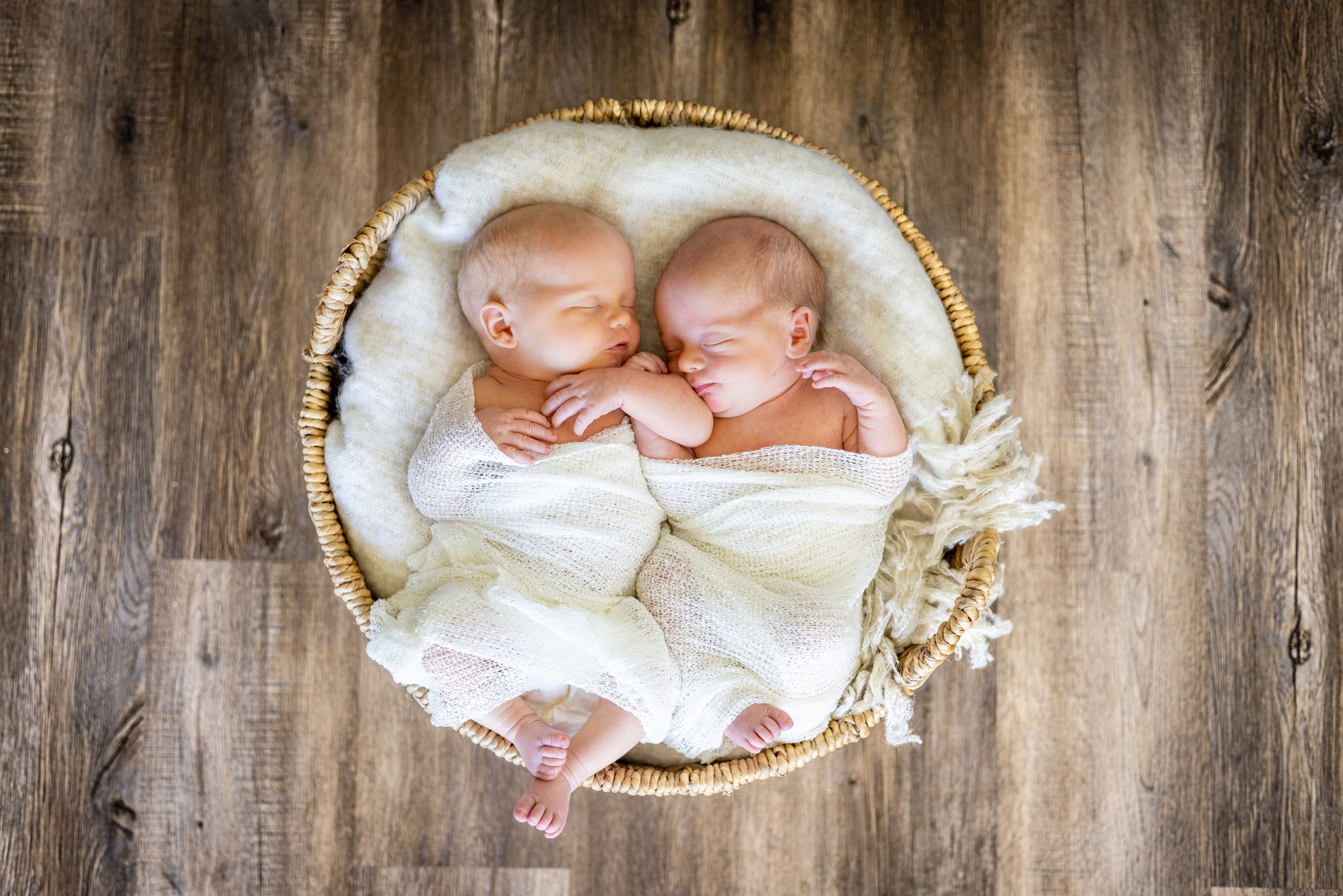 Sleeping newborn babies posed in woven baskets with soft white bedding.
