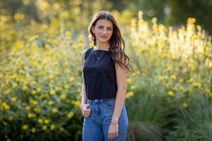 Woman in casual denim and navy top poses in a sunny meadow with yellow wildflowers during golden hour.