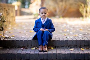 Young child in bright blue suit jacket poses on brick path during autumn.