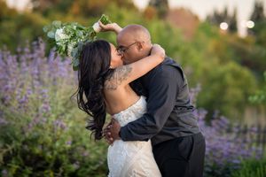 A couple shares a romantic moment surrounded by blooming purple flowers in an outdoor garden setting.