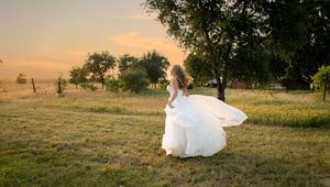 A bride in a flowing white dress poses in a golden field at sunset during a romantic outdoor photo session.