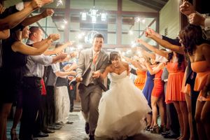 Wedding couple exits reception venue under glowing sparklers held by guests in a dimly lit corridor.