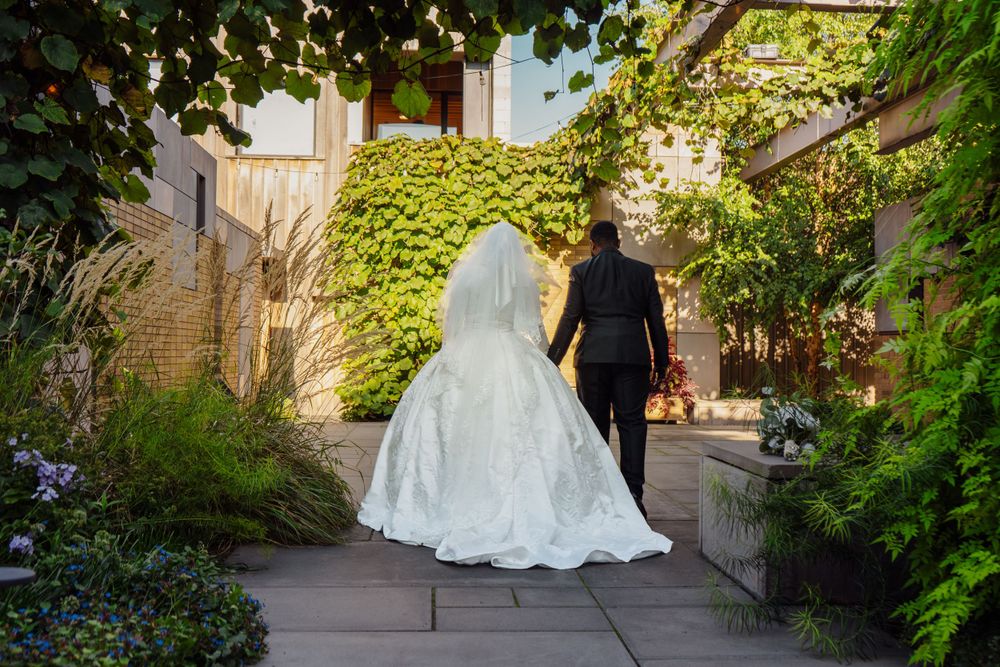 Muslim Wedding Photo of husband and wife holding hands and walking through their wedding venue's beautiful garden.