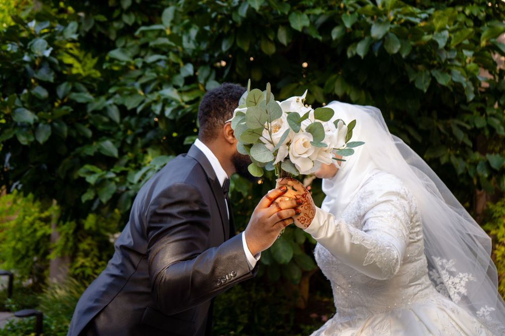Muslim Wedding Photo of husband and wife holding a bouquet up to the camera to cover their faces.