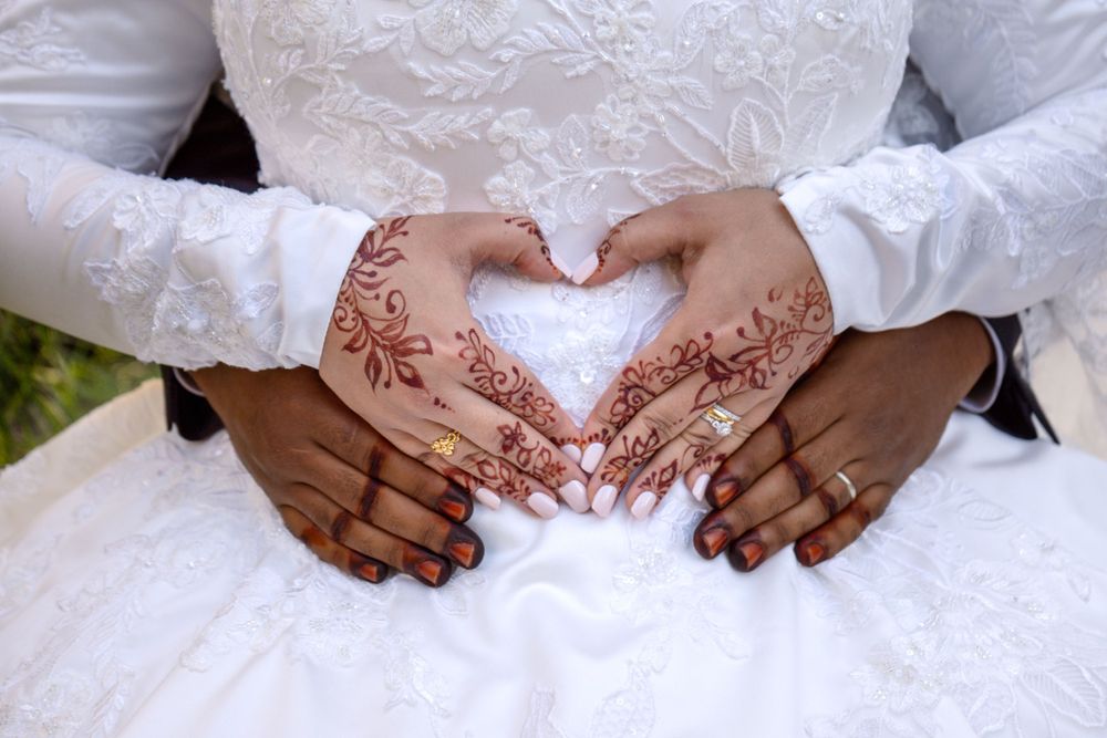 Wedding close-up photo of husband wrapping hands around the bride's torso as their henna-stained hands form a heart.