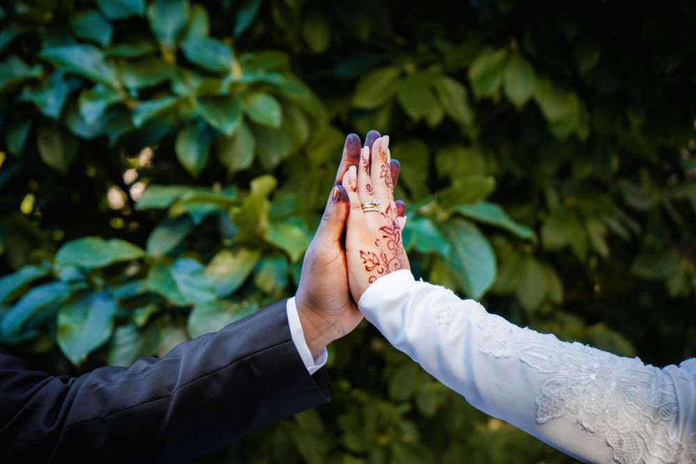 Close up of bride and groom's hand high-fiving. Their attire implies a mens suit and the bride's white embroidered gown.