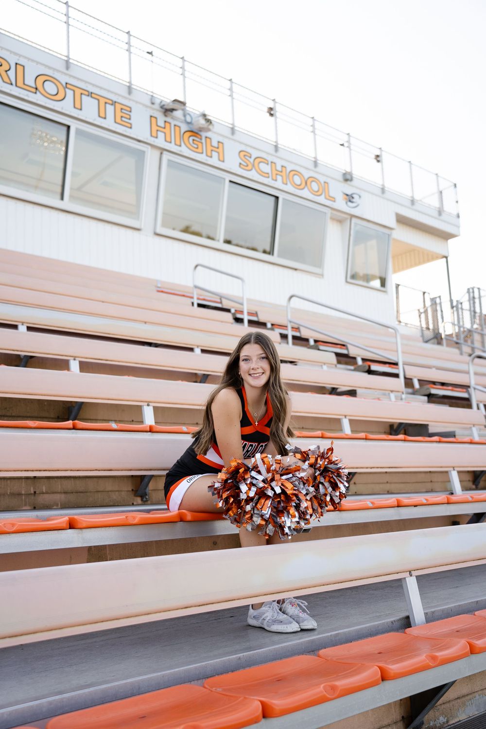 Cheerleader poses on orange bleachers during outdoor sports photoshoot.