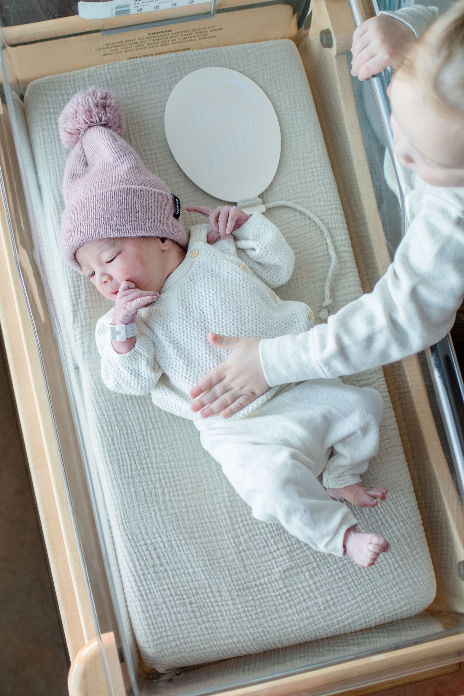 Overhead view of newborn in pink hat and white outfit lying on changing table.