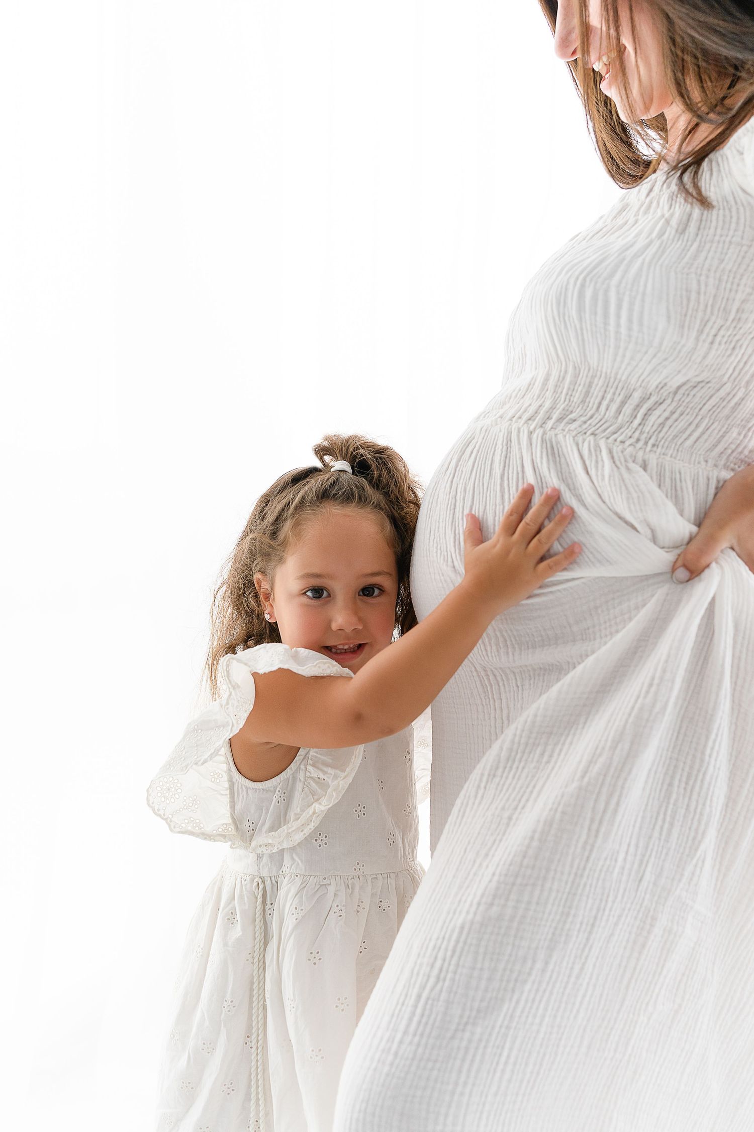 Mother in flowing white dress shares sweet moment with daughter during maternity session.