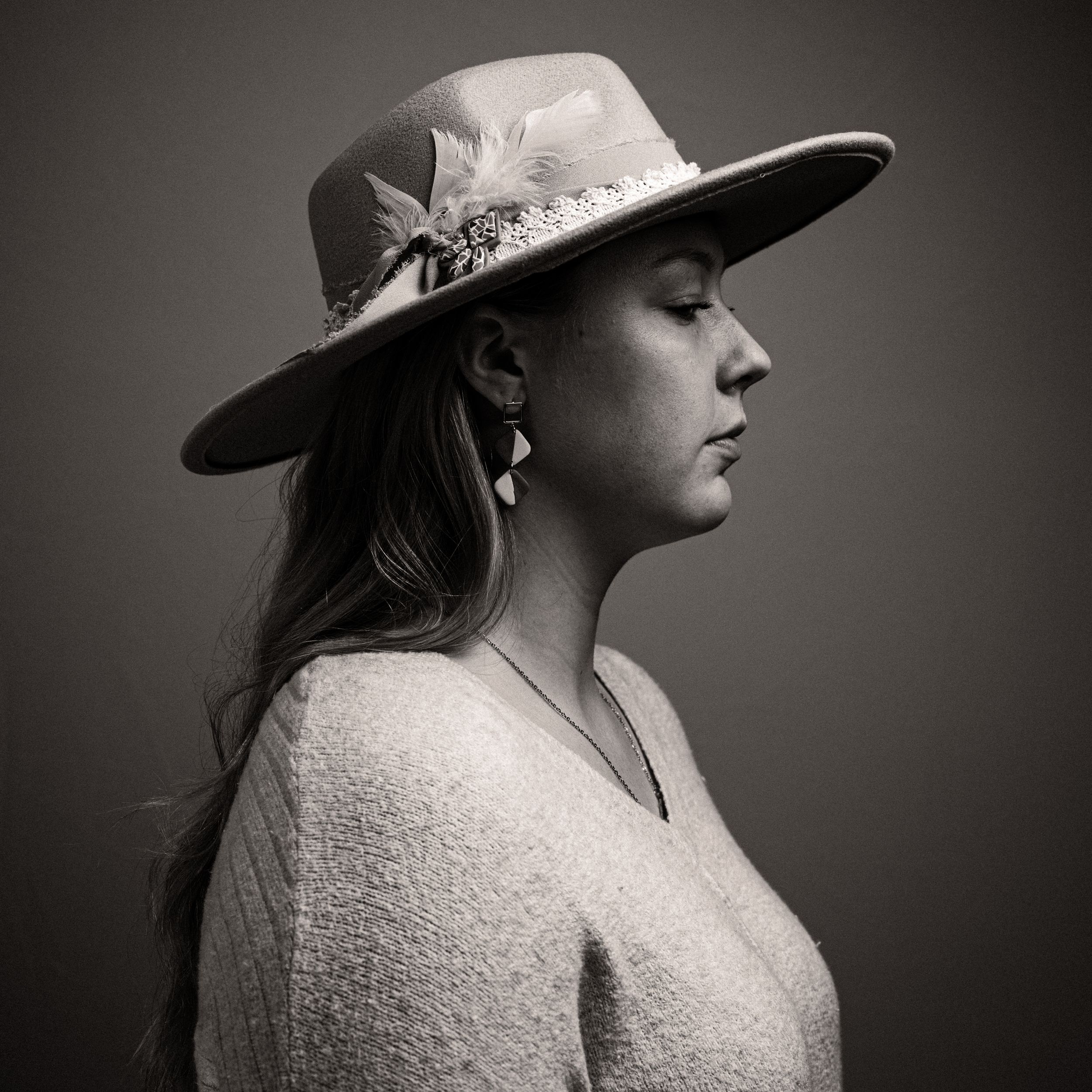 A black and white profile portrait of a woman wearing a wide-brim hat with feather detail.