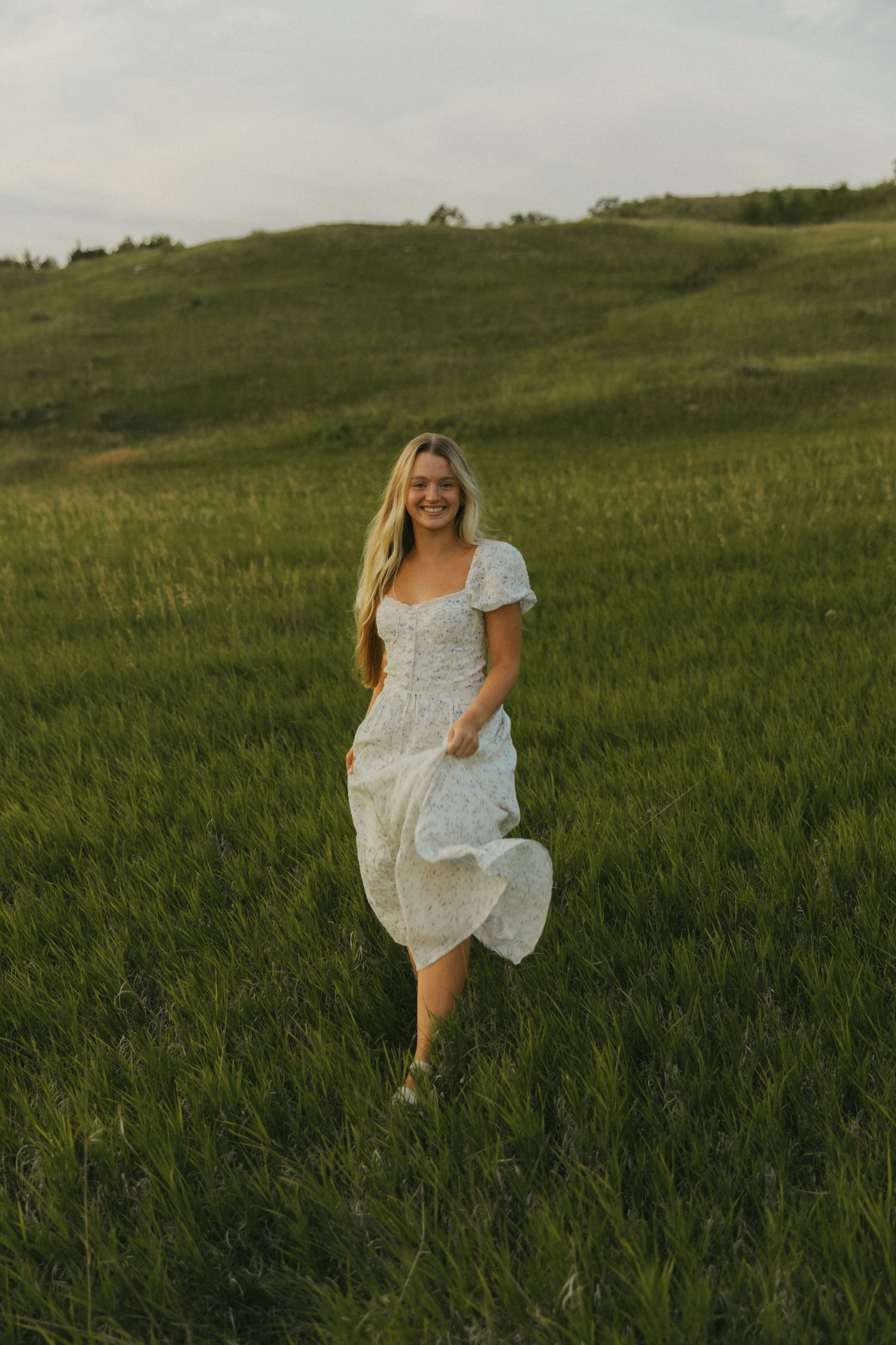 Woman in white sundress standing in green meadow during sunset.